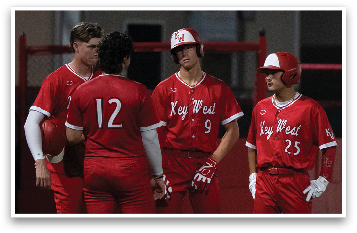 Four baseball players wearing red uniforms and white hats stand on a field. AI generated content