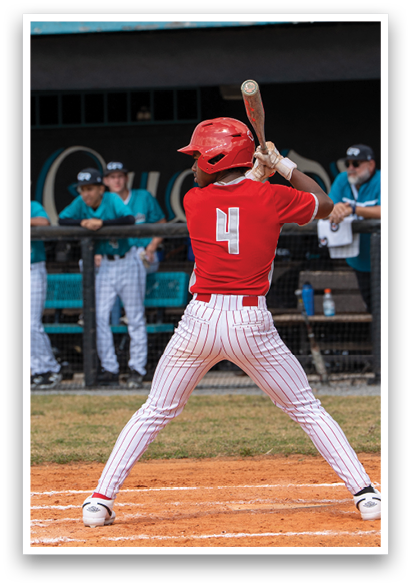 A baseball player is at bat, holding a bat and getting ready to swing. There are other players on the field, including one wearing a red shirt. A bench is visible in the background. AI generated content