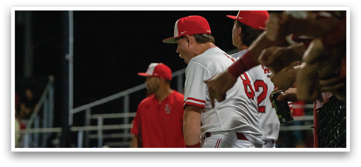 A group of baseball players are standing on the field, some of them wearing red and white uniforms. They are talking to each other, likely discussing their game strategy. The players are spread out across the field, with some standing closer to the foreground and others further back. A baseball bat can be seen in the hands of one of the players, indicating that they are ready to play. AI generated content