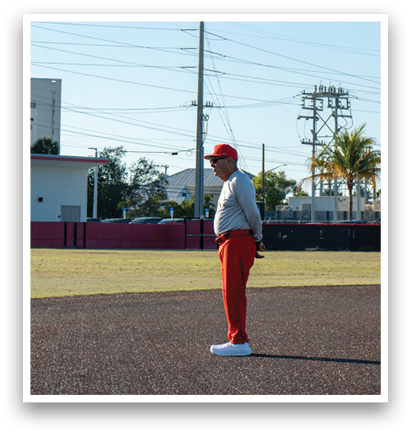 A man in a red shirt and red pants stands on a baseball field. AI generated content