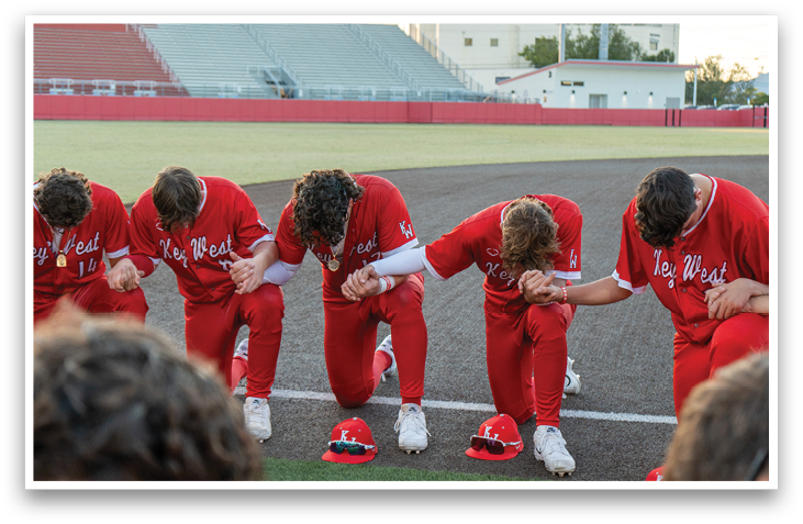 Baseball players in red uniforms are kneeling on the field, praying before a game. AI generated content