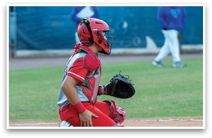 A baseball player in a red and grey uniform is kneeling on the ground with a catcher's mitt on his hand. AI generated content