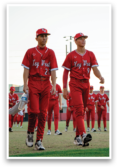 Two baseball players in red uniforms walk on a field. AI generated content