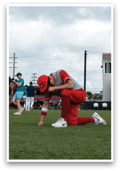 A baseball player is kneeling on the field, wearing a red and white uniform. AI generated content
