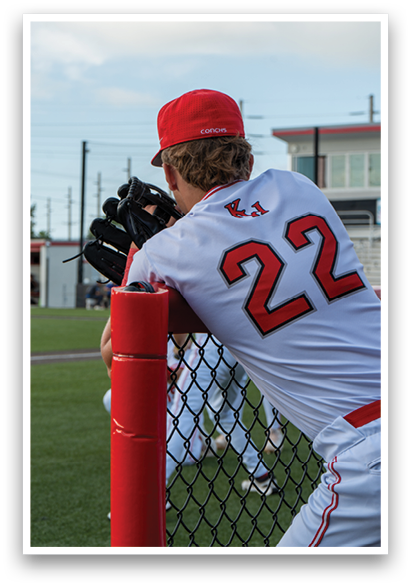 A baseball player wearing a red hat and white jersey is leaning on a fence. AI generated content