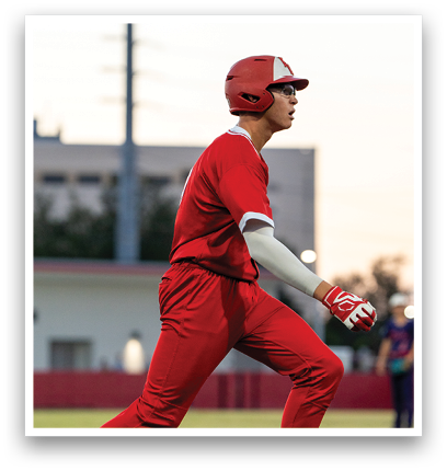 A baseball player in a red jersey and red pants is running towards home plate. Description generated by AI
