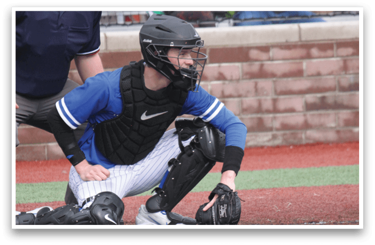 A baseball catcher is kneeling on the ground wearing a blue shirt and black pants. AI generated content