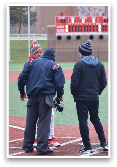 Three people are standing on a baseball field, engaged in conversation. One person is wearing a red hat, and another is wearing a blue hat. They are all standing near home plate. AI generated content
