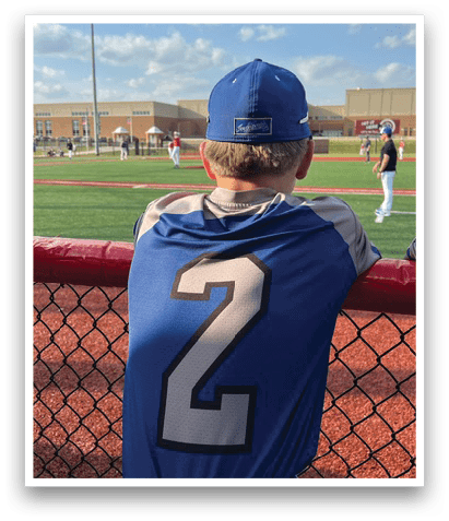 A baseball player wearing a blue and white jersey with the number 2 on the back is leaning against a fence. AI generated content