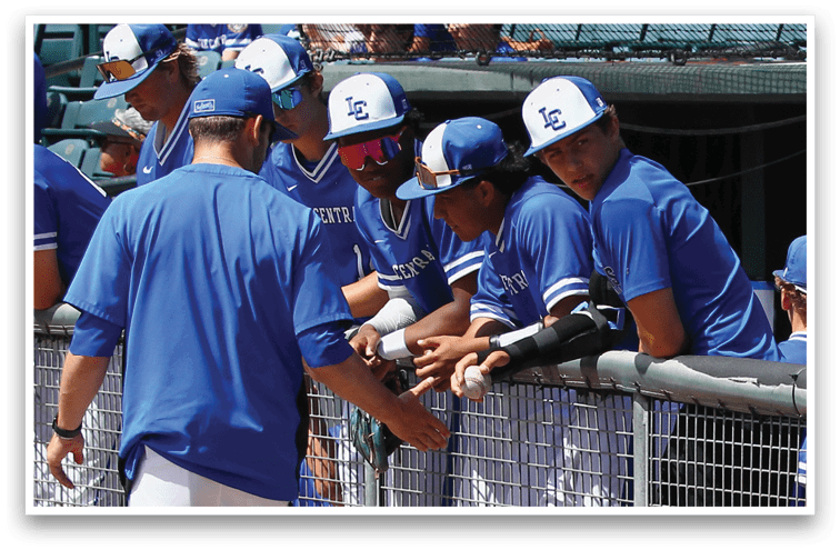 A group of people wearing blue baseball uniforms and caps are gathered around a fence, with one person handing a baseball to another. Description generated by AI