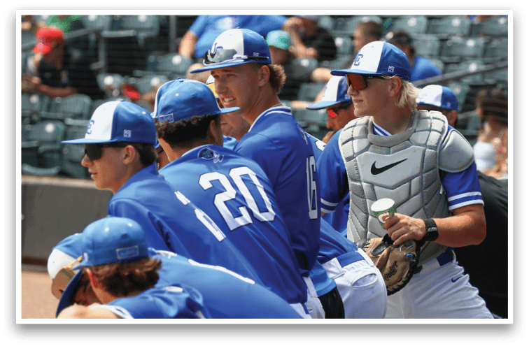 People in blue baseball uniforms are gathered together, with one person wearing catcher's gear holding a cup and glove. Description generated by AI