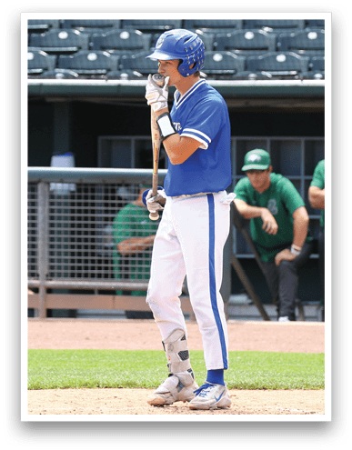 A person wearing a blue baseball uniform and helmet is standing on a baseball field holding a bat, preparing to bat. Description generated by AI