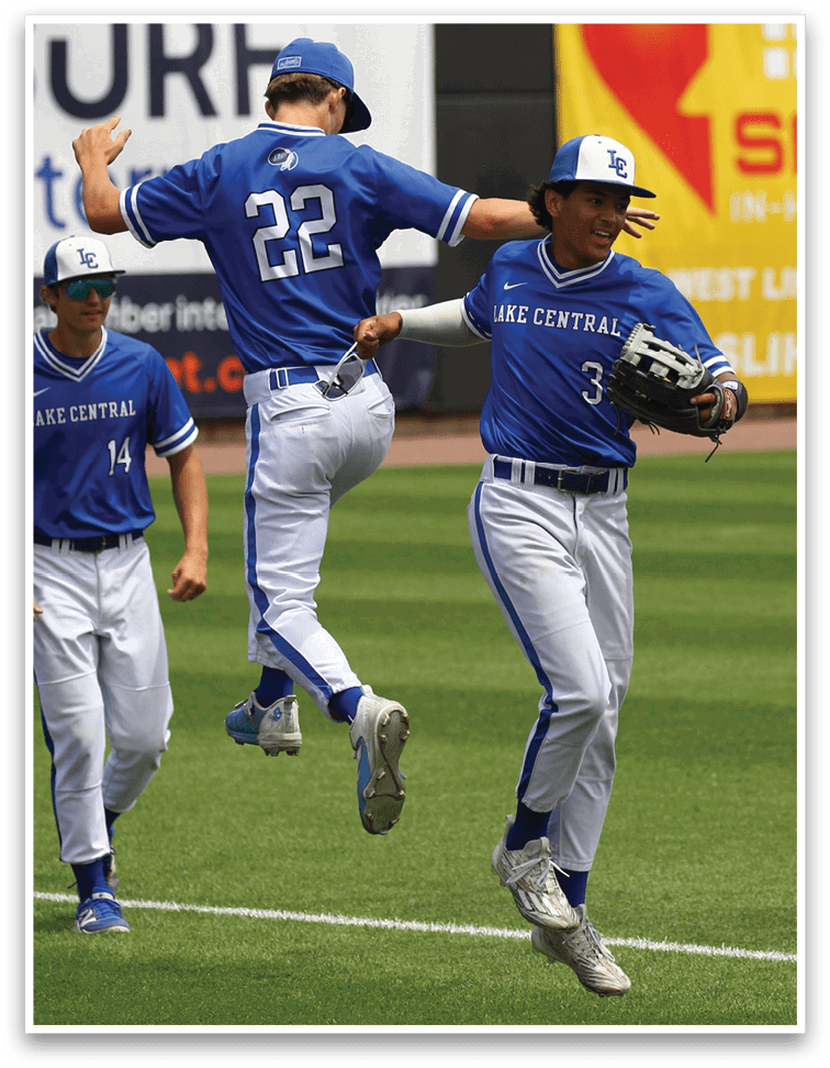 Two people in blue and white baseball uniforms are celebrating on a baseball field with one person jumping and the other extending an arm. Description generated by AI