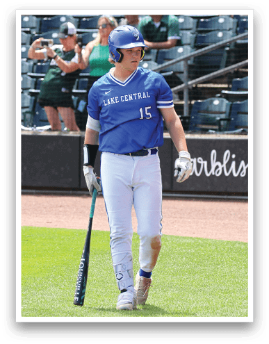 A person in a blue Lake Central sports uniform and helmet is standing on a baseball field holding a bat with spectators in the background. Description generated by AI