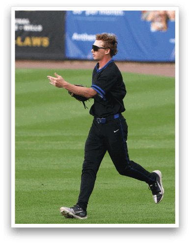 A person wearing a black sports uniform is reaching out with a glove to catch a baseball in mid-air on a grassy field. Description generated by AI