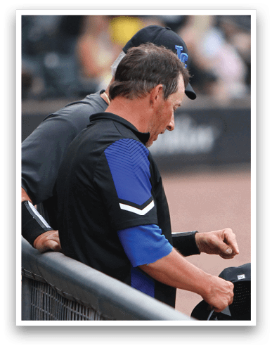 Two people in sports attire stand near a railing, with one holding a black cap and the other wearing a black cap with a logo. Description generated by AI