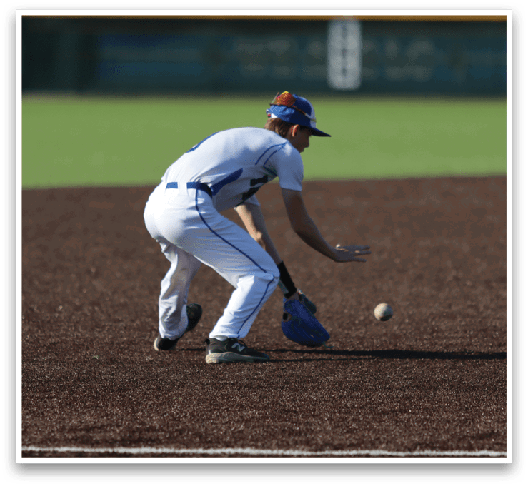 A baseball player in a white uniform is bending over to catch a ball. AI generated content