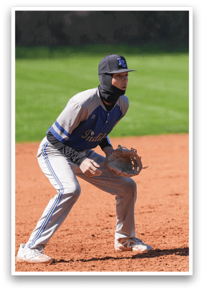 A baseball player is crouched on the field, wearing a blue and white uniform and a blue hat. He is holding a baseball glove, ready to catch the ball. The scene takes place on a baseball field, with a scoreboard visible in the background. AI generated content