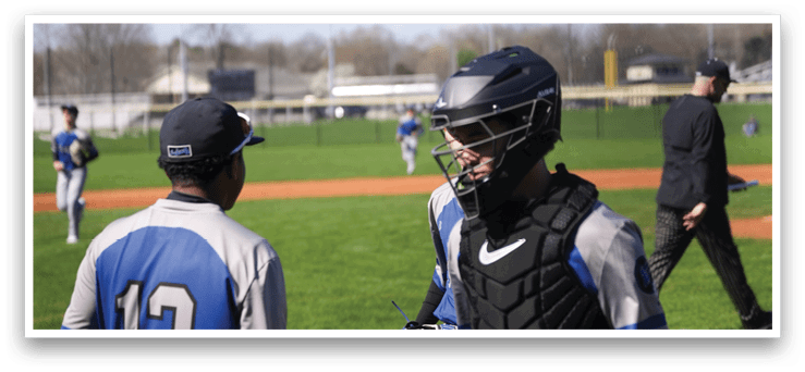 Two baseball players wearing blue and grey uniforms are talking to each other on the field. One player is wearing a helmet and holding a baseball bat. AI generated content