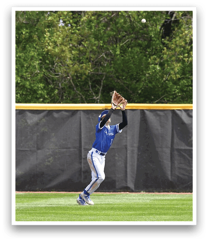 A baseball player wearing a blue shirt and white pants is leaping in the air to catch a ball. AI generated content