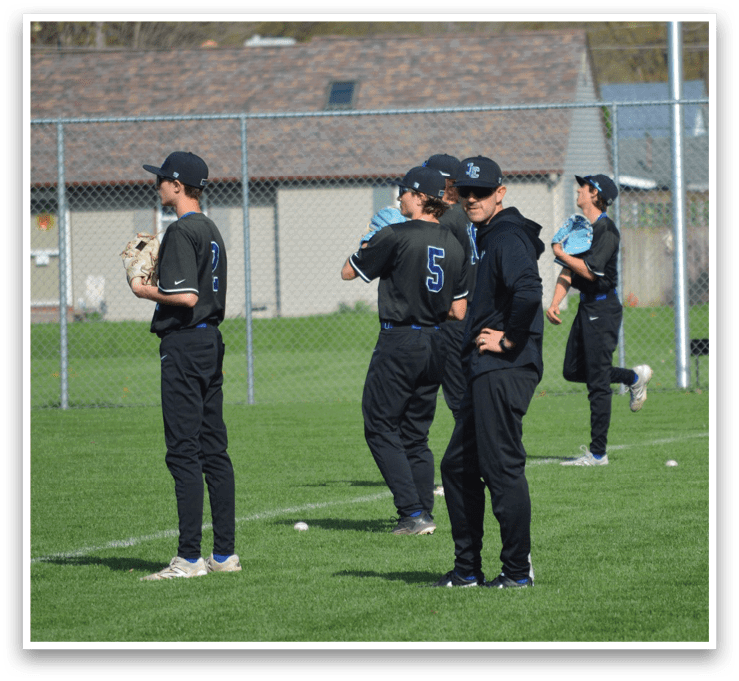 A group of young men are standing on a baseball field, wearing baseball uniforms and holding baseball gloves. They are likely waiting for their turn to bat or practice their fielding skills. AI generated content