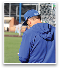 A man wearing a blue jacket and blue hat is standing on a baseball field. AI generated content
