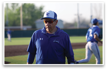 A man wearing a blue and white baseball cap and jacket stands on a baseball field. AI generated content
