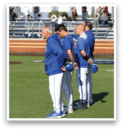 A group of men wearing blue and white uniforms stand on a baseball field. Description generated by AI
