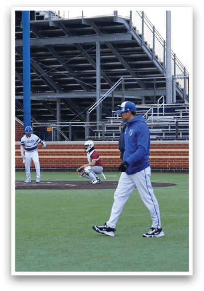 A baseball field with a man walking on it. Description generated by AI