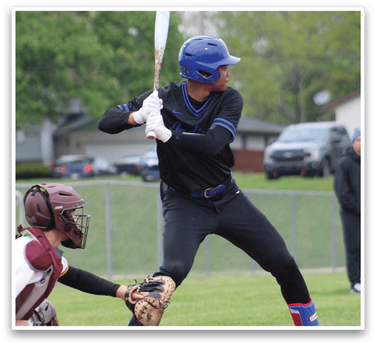 A baseball player in a black shirt and blue hat is swinging a bat. Description generated by AI