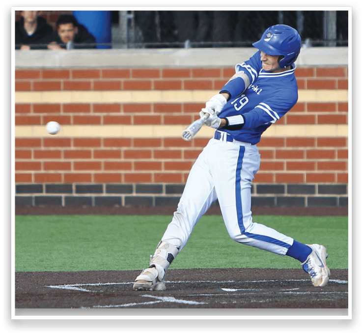 A baseball player in a blue and white uniform is swinging a bat at a ball. Description generated by AI