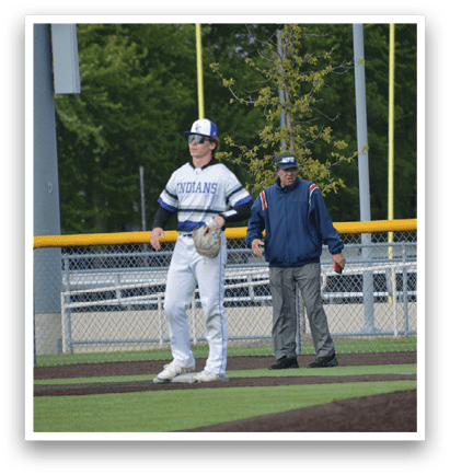 A baseball player with a white uniform and blue hat standing on the field. Description generated by AI
