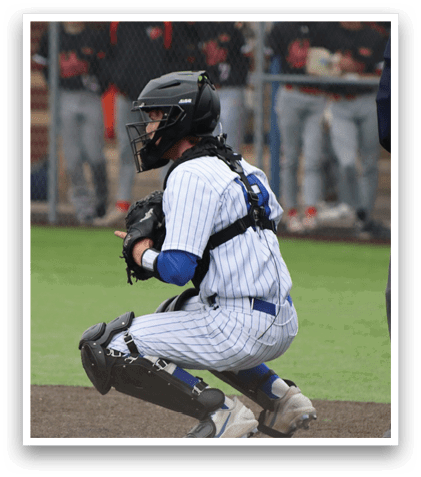A baseball catcher is squatting down in front of a fence. Description generated by AI