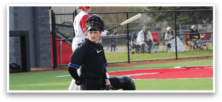 A baseball player in a black shirt and black pants squatting behind home plate. Description generated by AI