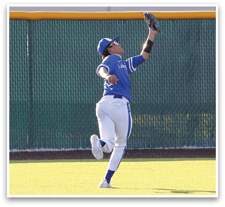 A baseball player wearing a blue and white uniform catching a ball. Description generated by AI