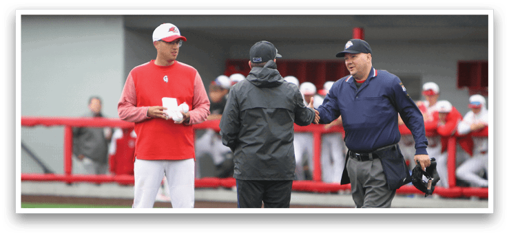 A man wearing a red shirt and white pants is talking to an umpire. Description generated by AI