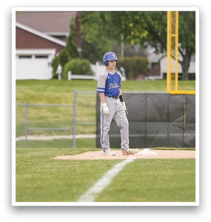 A baseball player in a blue helmet and white uniform stands on a base. Description generated by AI