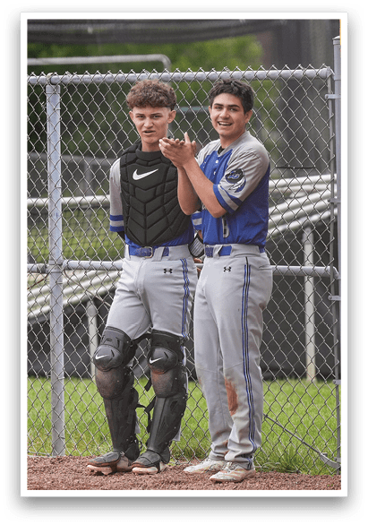 Two baseball players standing next to a fence. Description generated by AI