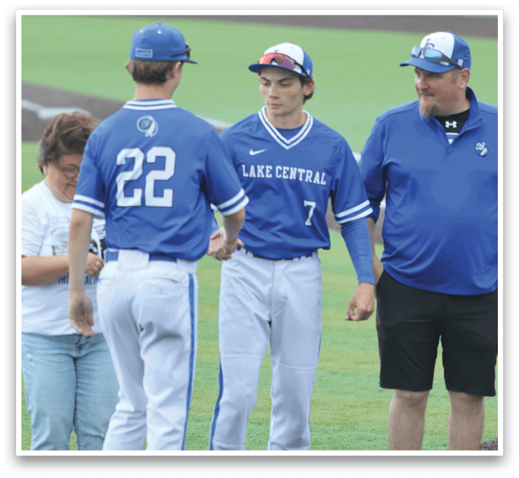 Two baseball players shake hands with a man in a blue shirt. Description generated by AI