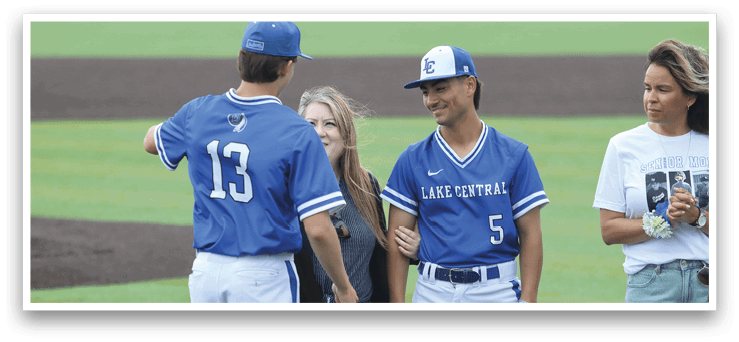 Two men wearing blue shirts and white pants stand on a field. Description generated by AI