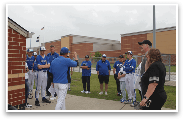 A group of people wearing blue shirts and white pants are standing on a sidewalk. Description generated by AI