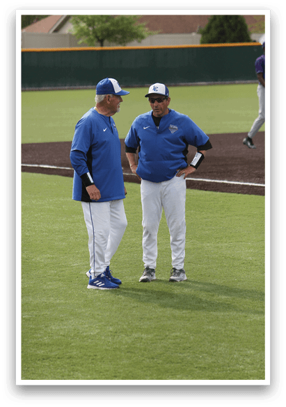 Two men wearing blue shirts and white pants standing on a baseball field. Description generated by AI