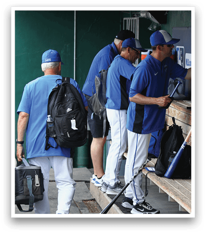 A group of men wearing blue shirts and white pants are standing around a bench. Description generated by AI