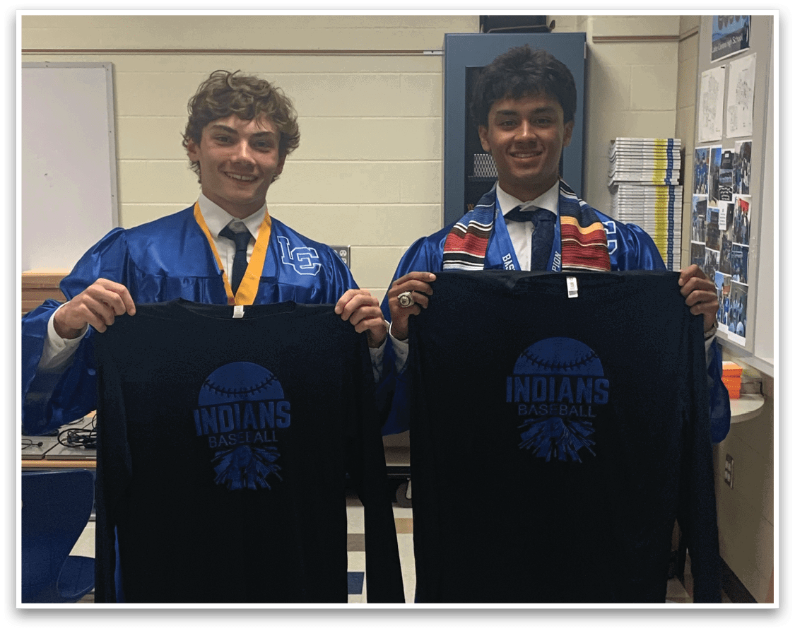 Two young men wearing blue robes and holding up black shirts with the word Indians on them. Description generated by AI