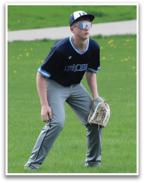 A young man in a blue shirt and grey pants is playing baseball in a field. He is holding a baseball glove and appears to be ready to catch a ball. AI generated content