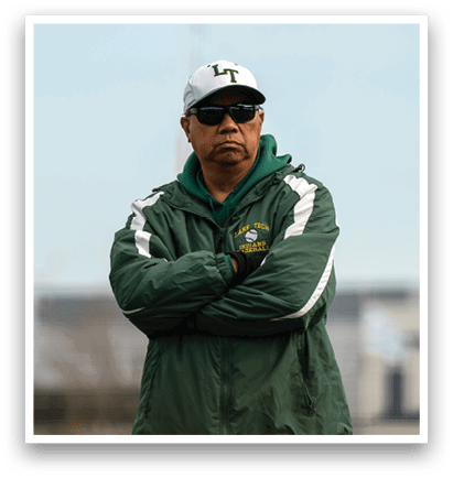 A man wearing a green jacket and a white cap stands on a baseball field. AI generated content