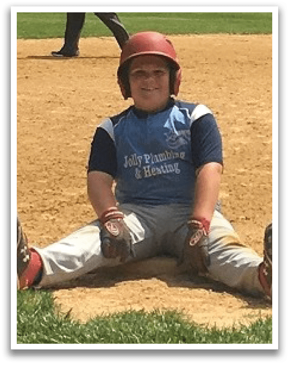 A young boy wearing a baseball uniform is sitting on the ground with his legs spread out. AI generated content