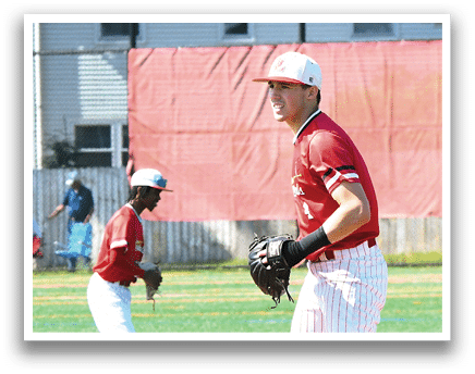 A baseball player in a red shirt and white pants stands on a mound. Description generated by AI