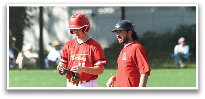 Two men wearing red shirts and white pants are standing on a baseball field. Description generated by AI