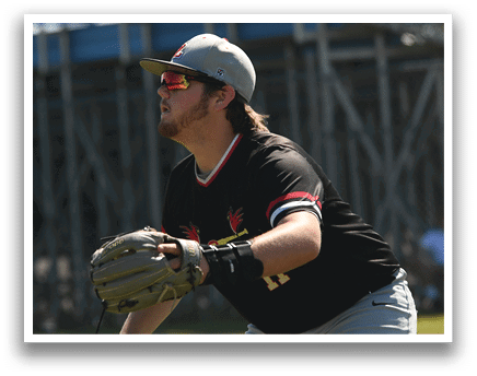 A baseball player in a red shirt and white pants stands on a mound. Description generated by AI